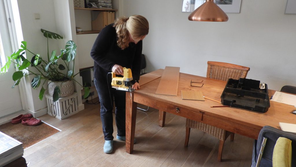 Nicole saws a plank with a jigsaw.